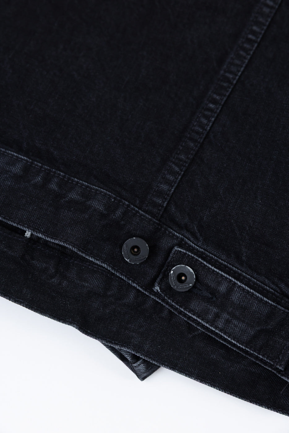 Close-up of black denim jacket hem, showing front side with button and seam details.