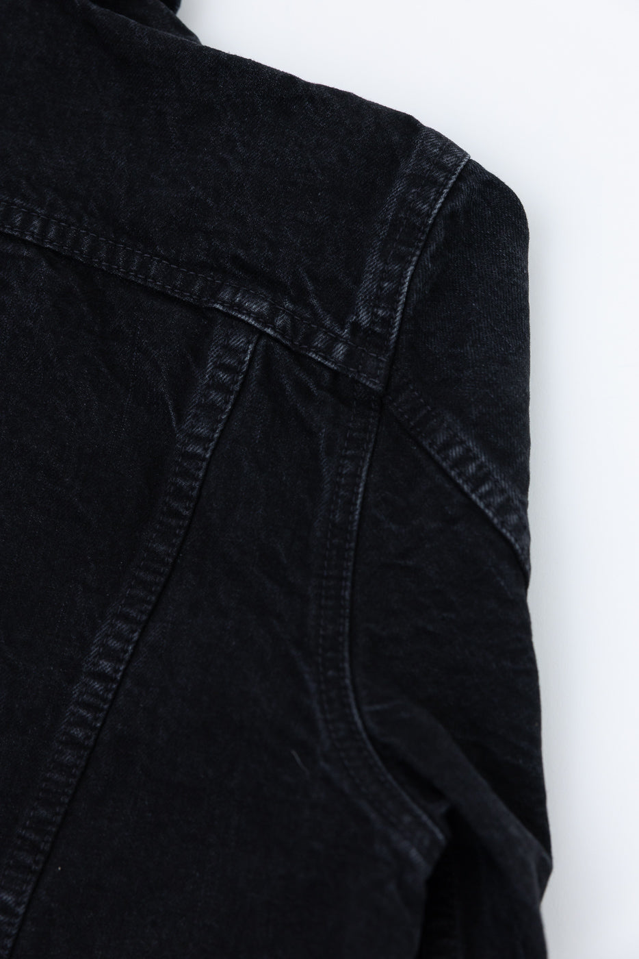Close-up of back shoulder seam and upper sleeve on black washed denim jacket