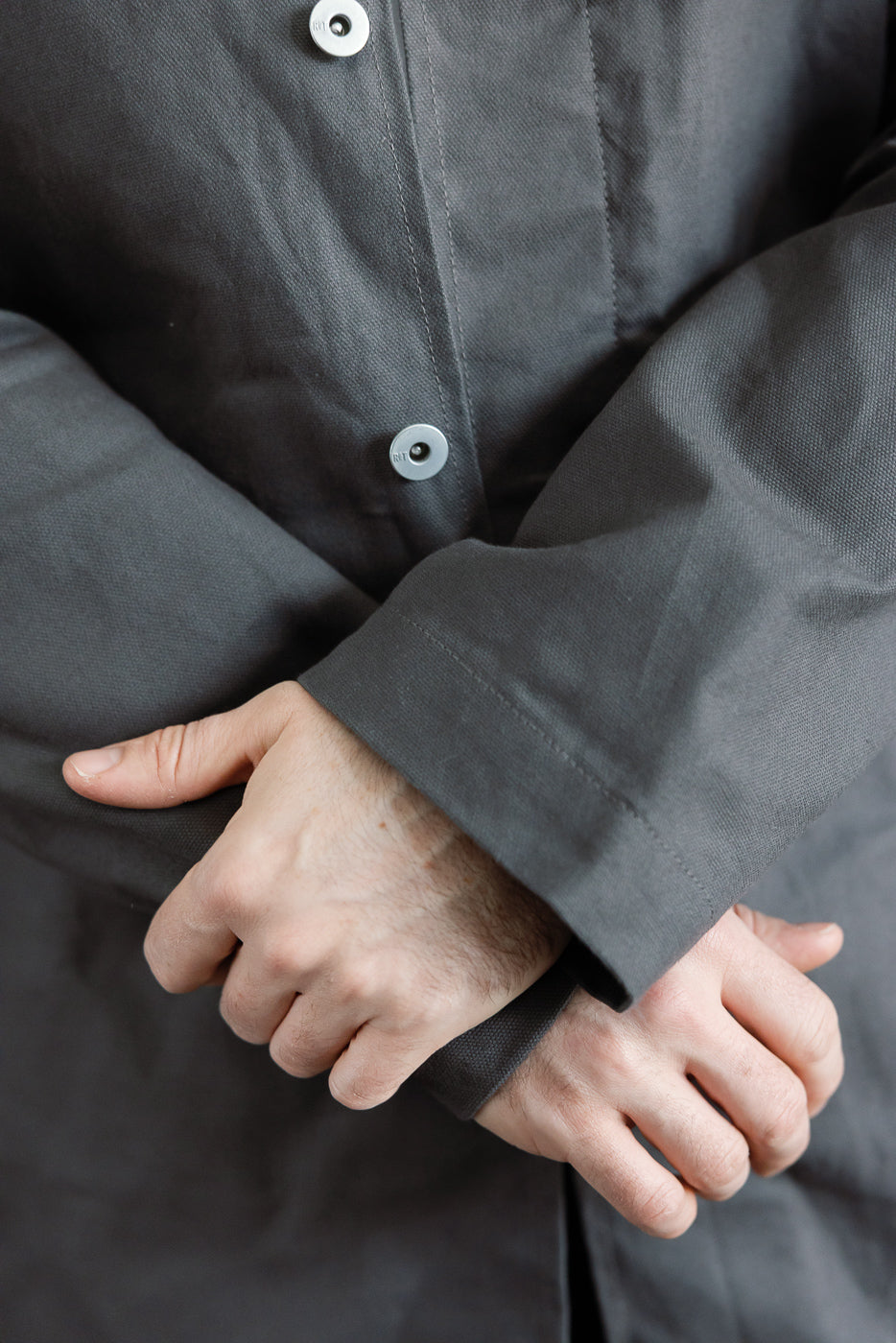 Close-up of front torso and sleeves of grey dry waxed canvas trench coat on a male model, highlighting button and cuff details.