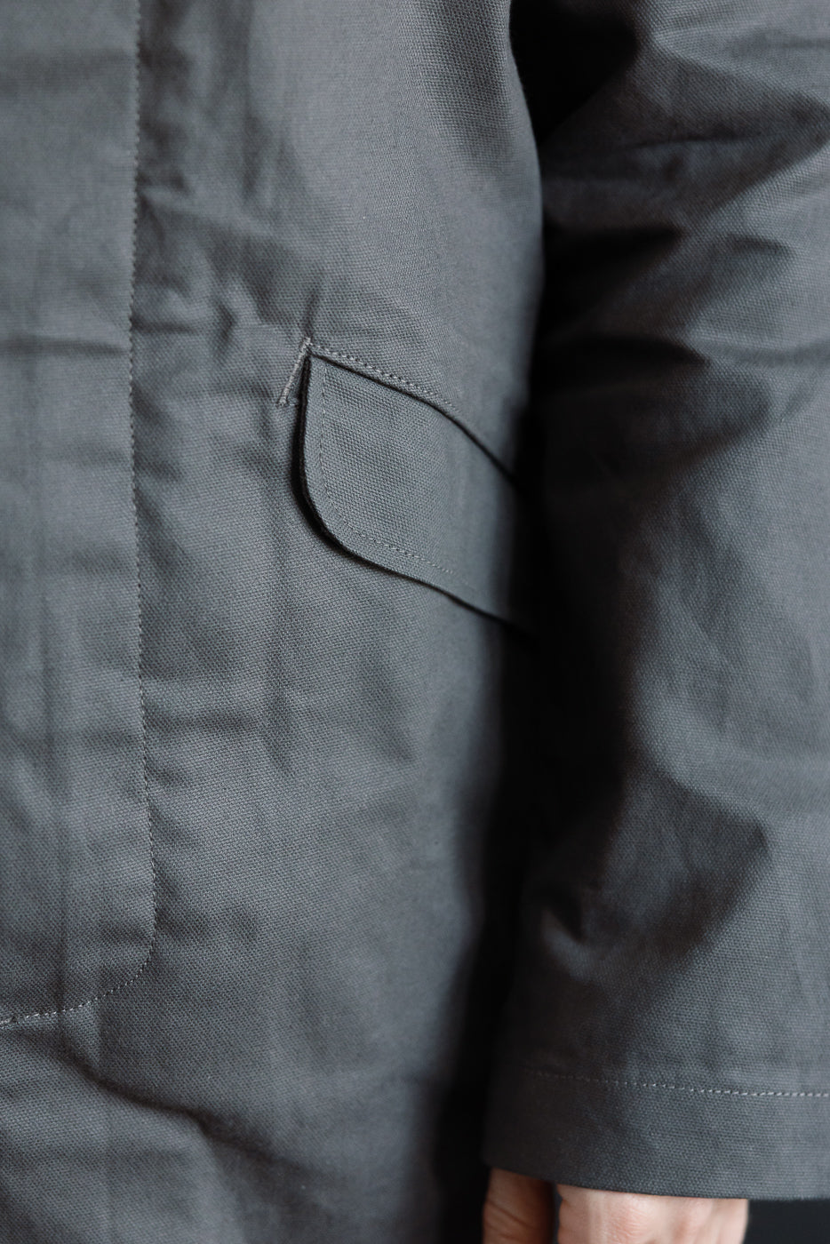 Close-up of side pocket on grey dry waxed canvas trench coat, showing texture and stitching.