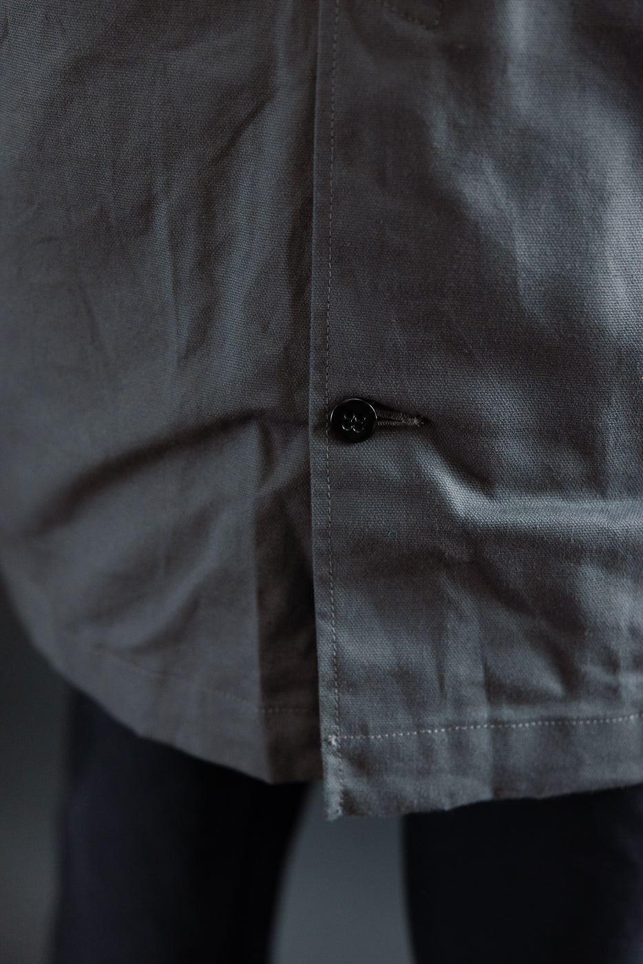 Close-up of lower front hem and side button detail on grey waxed canvas trench coat