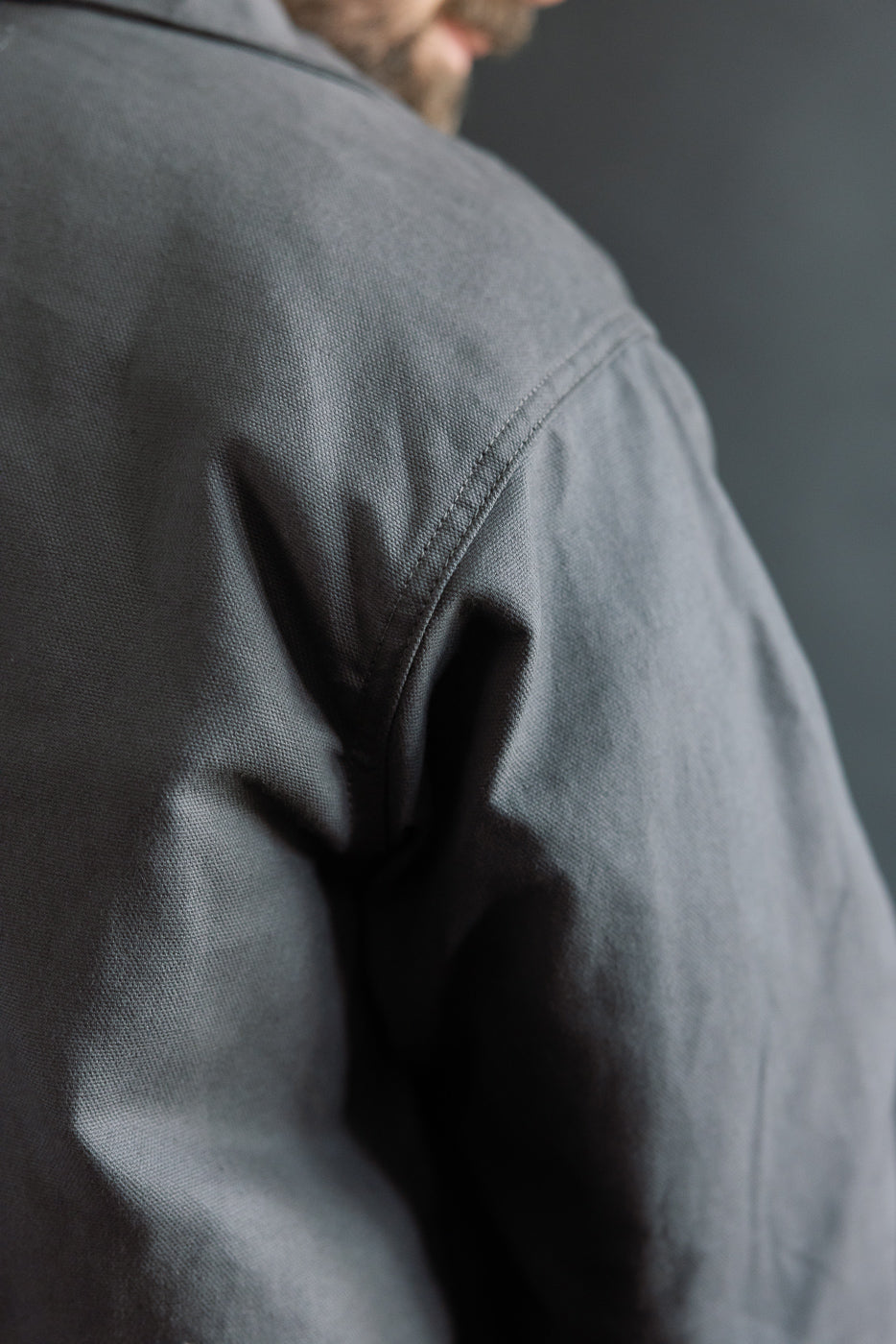Close-up of shoulder seam and fabric texture on men's grey dry waxed canvas trench coat, left side.