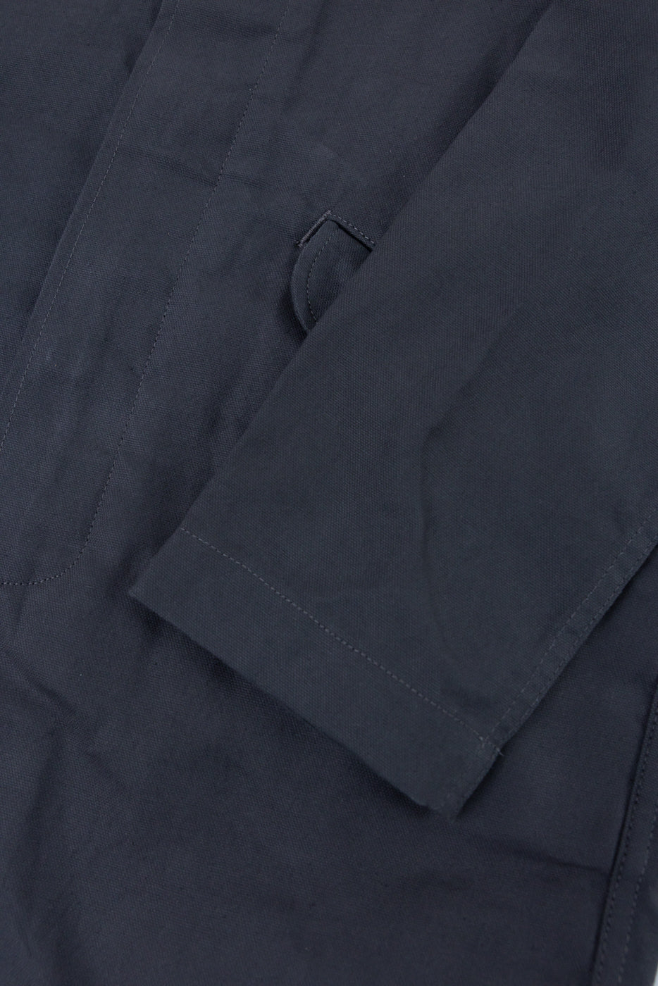 Close-up of grey trench coat sleeve and front pocket, highlighting dry waxed canvas texture.