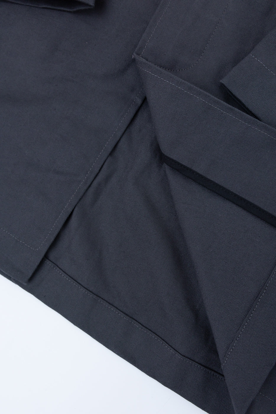 Close-up of the front hem and pocket flap details on a grey waxed canvas trench coat.