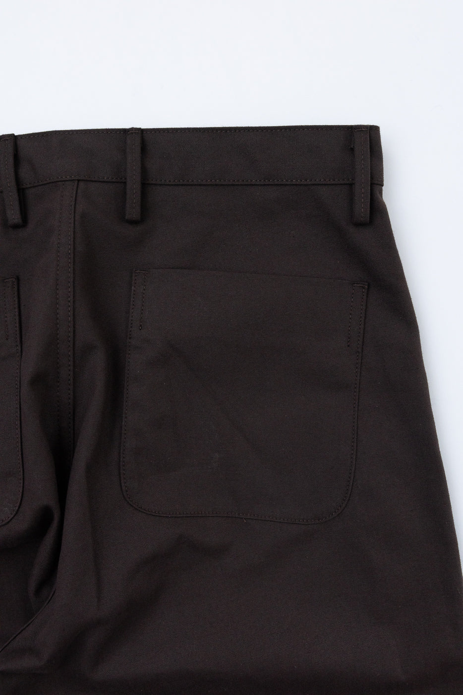 Close-up of the back of brown trousers showing a rear pocket and waistband loops.