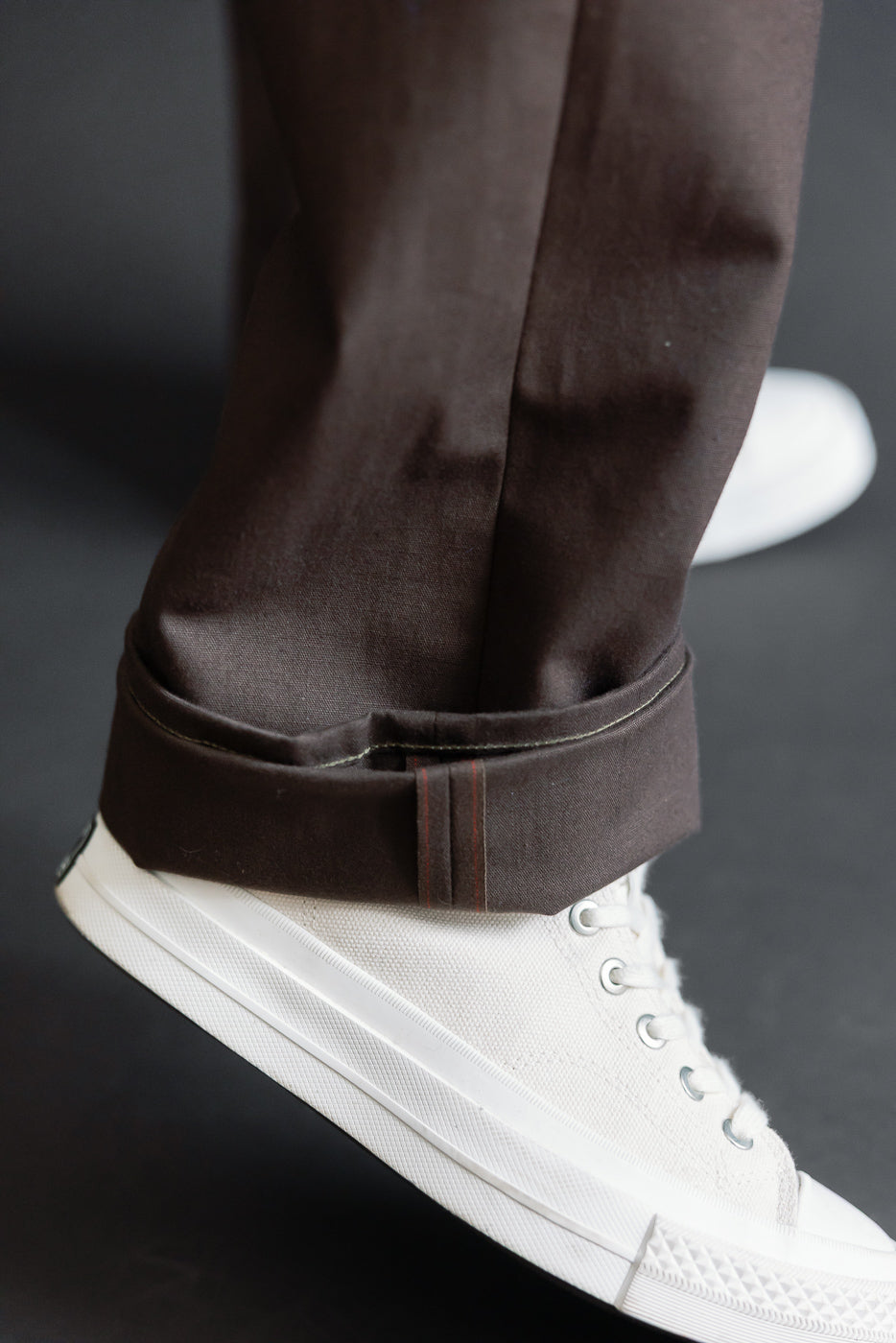 Close-up of a male model's brown selvedge denim pant cuff and white sneakers.