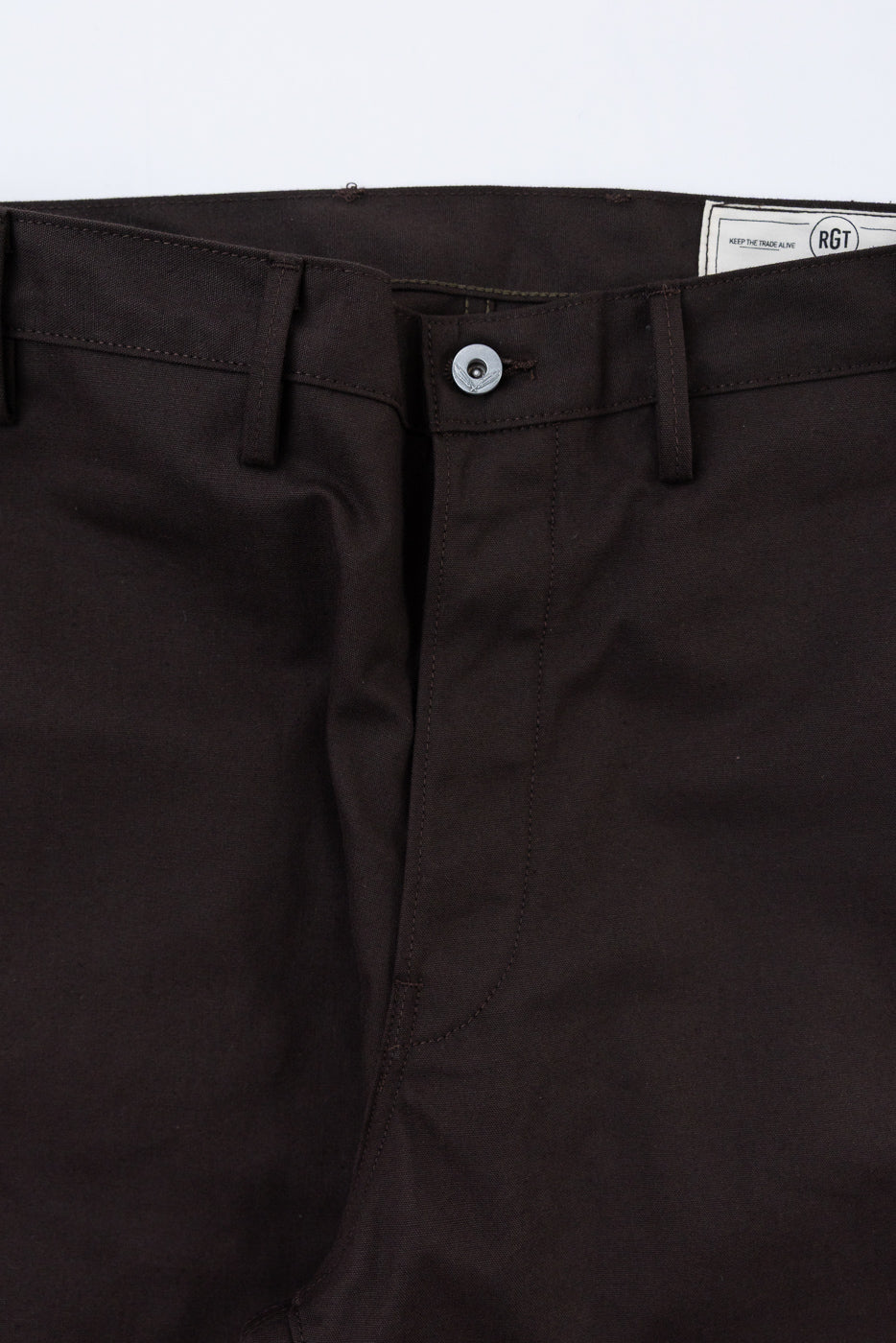 Close-up of the front waist and button closure of brown RGT trousers showing fabric texture.