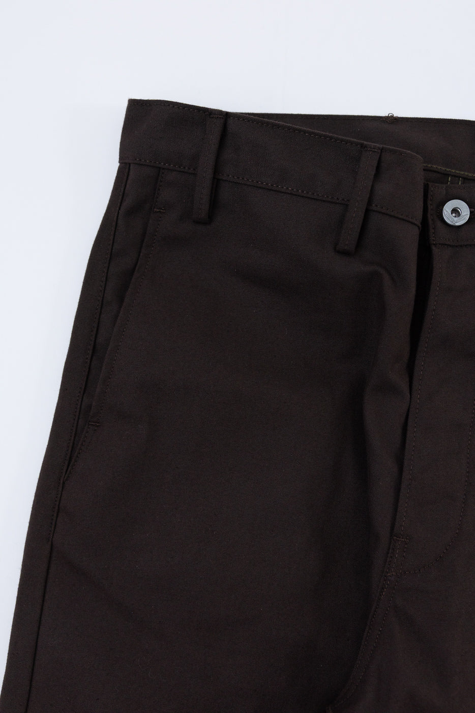 Close-up of the front waist and pocket area of dark brown trousers, showing the button and belt loops.