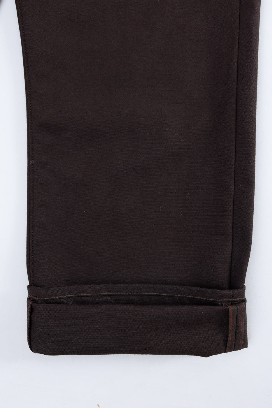 Close-up of the bottom hem and cuffed leg of dark brown cotton trousers.