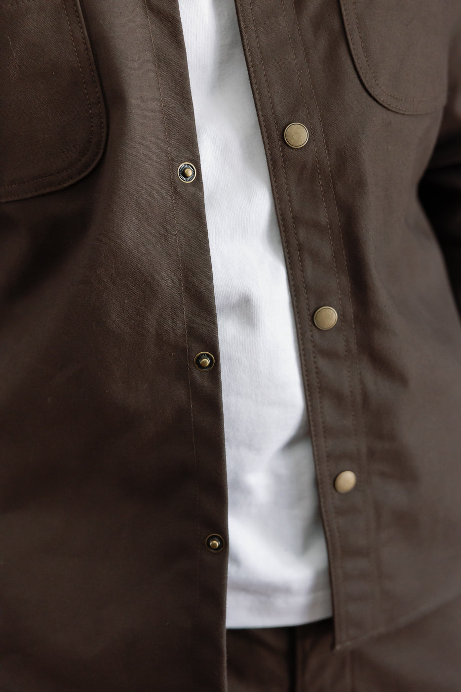 Close-up front view of brown canvas jacket showing metal snap button details.
