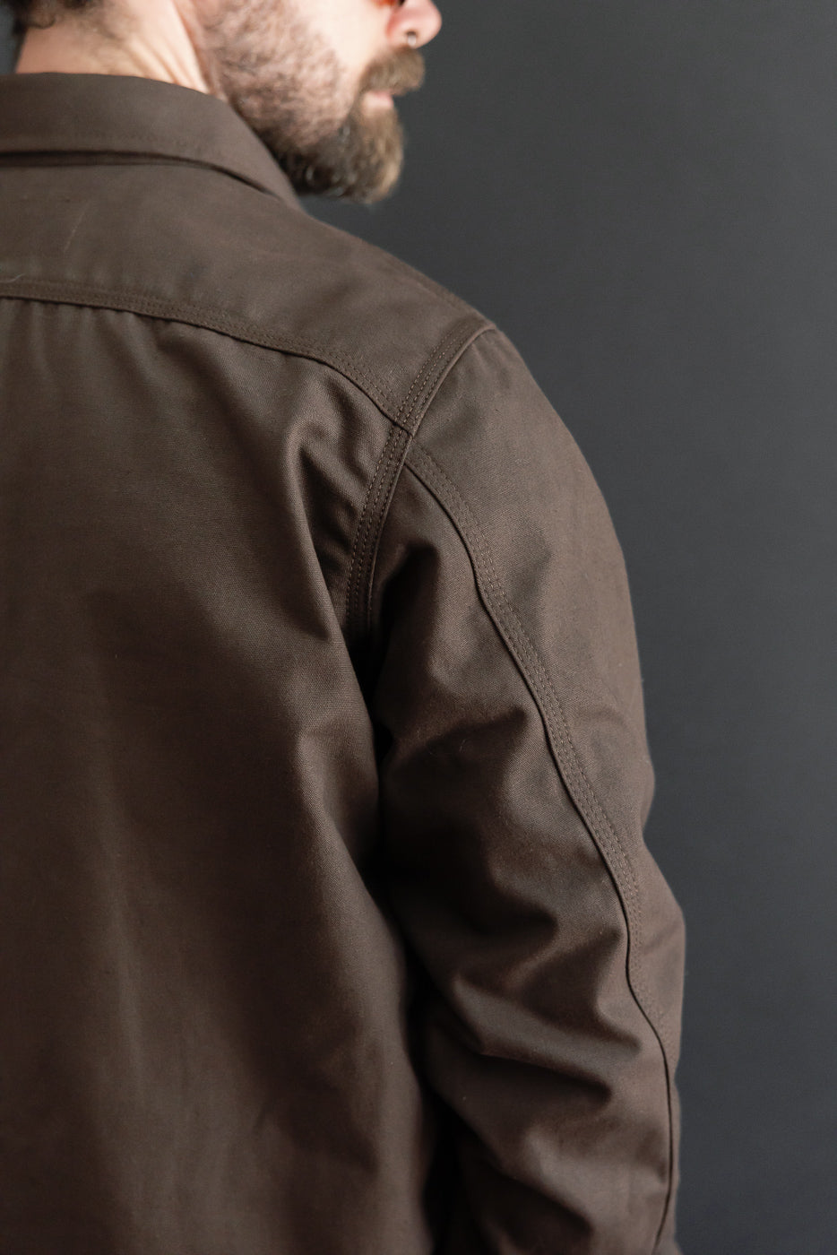 Close-up of the back and right side of a brown canvas jacket on a male model, 5'9