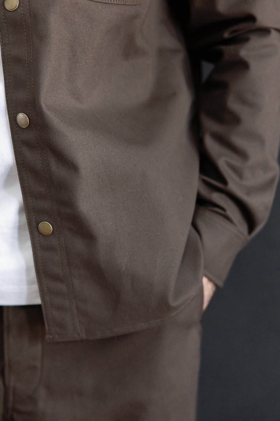Close-up of the left front of a brown jacket with brass snaps on a male model, 5'9