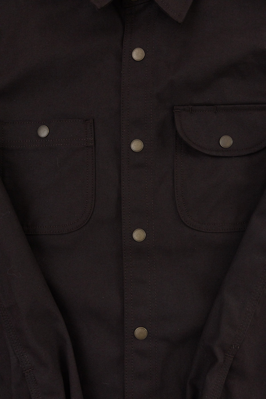 Close-up front view of a dark brown button-down shirt showing snap buttons and chest pockets.