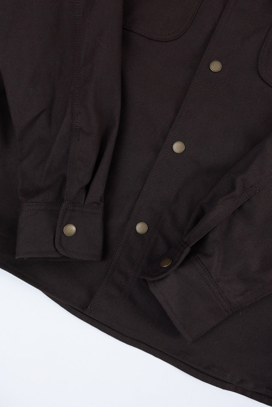 Close-up front view of dark brown button-down shirt showing metal snap buttons and fabric texture.