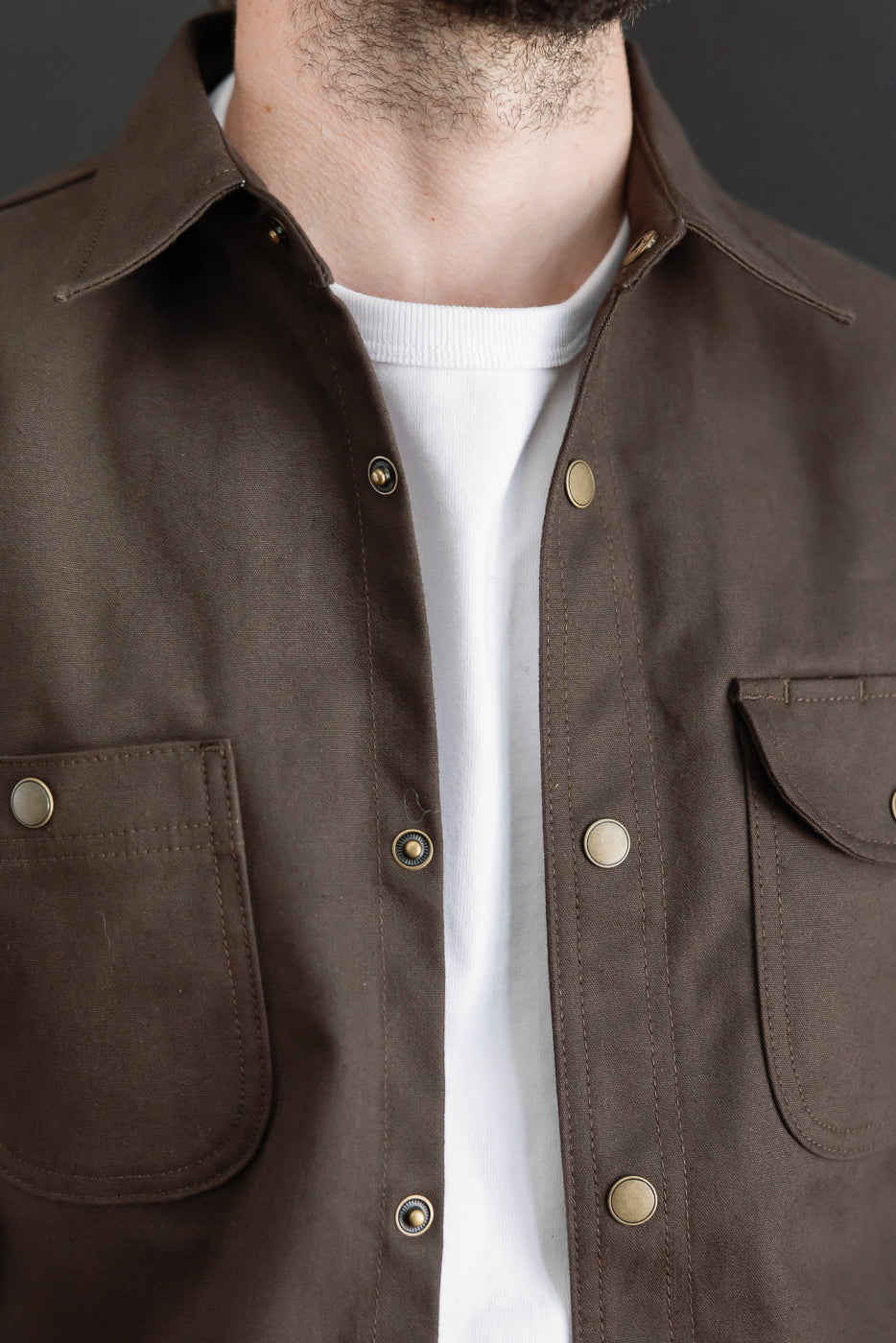Close-up front view of a brown button-down shirt featuring metal snap buttons and chest pockets.