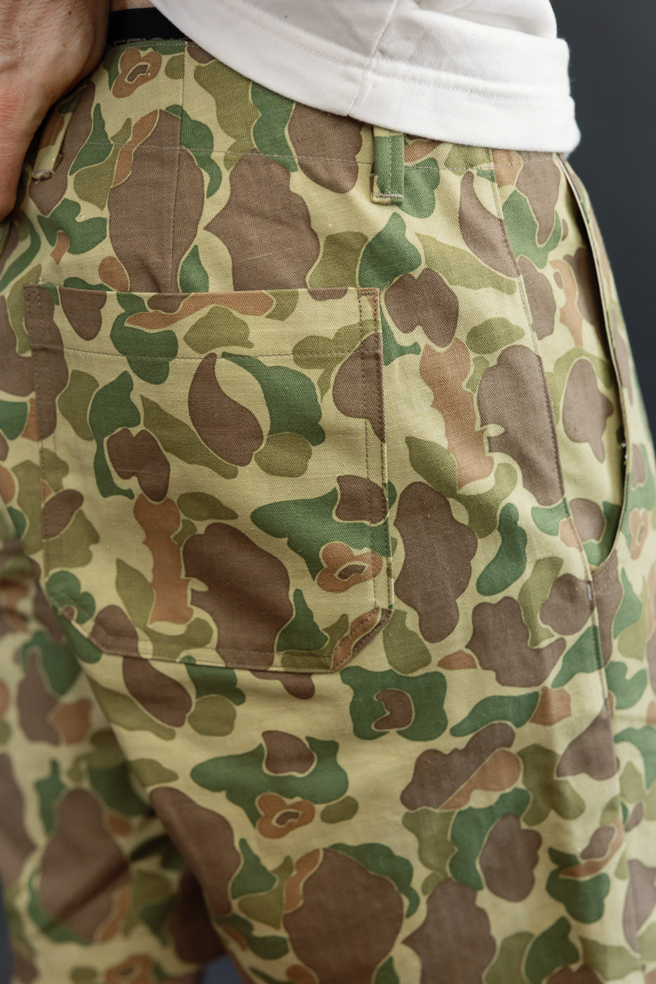 Close-up of male model's back pocket on camo pants, showcasing fabric texture and stitching detail.