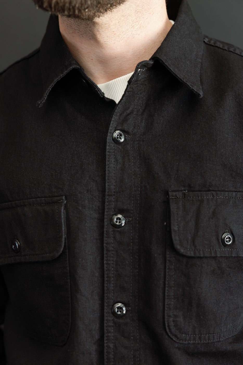 Close-up front view of black shirt with buttons and chest pockets, worn by male model