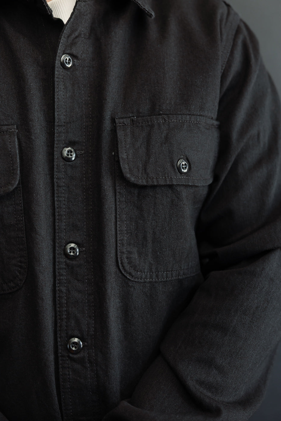 Close-up front view of black shirt with buttons and chest pocket, worn by male model
