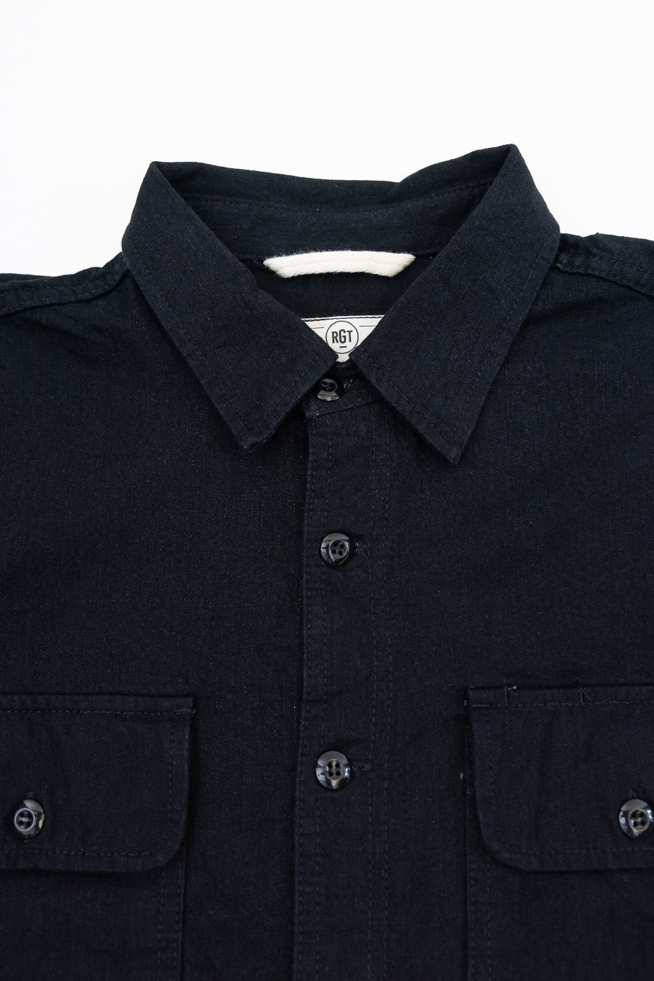 Close-up front view of dark denim shirt with button details, collar, and RGT tag, worn by male model.