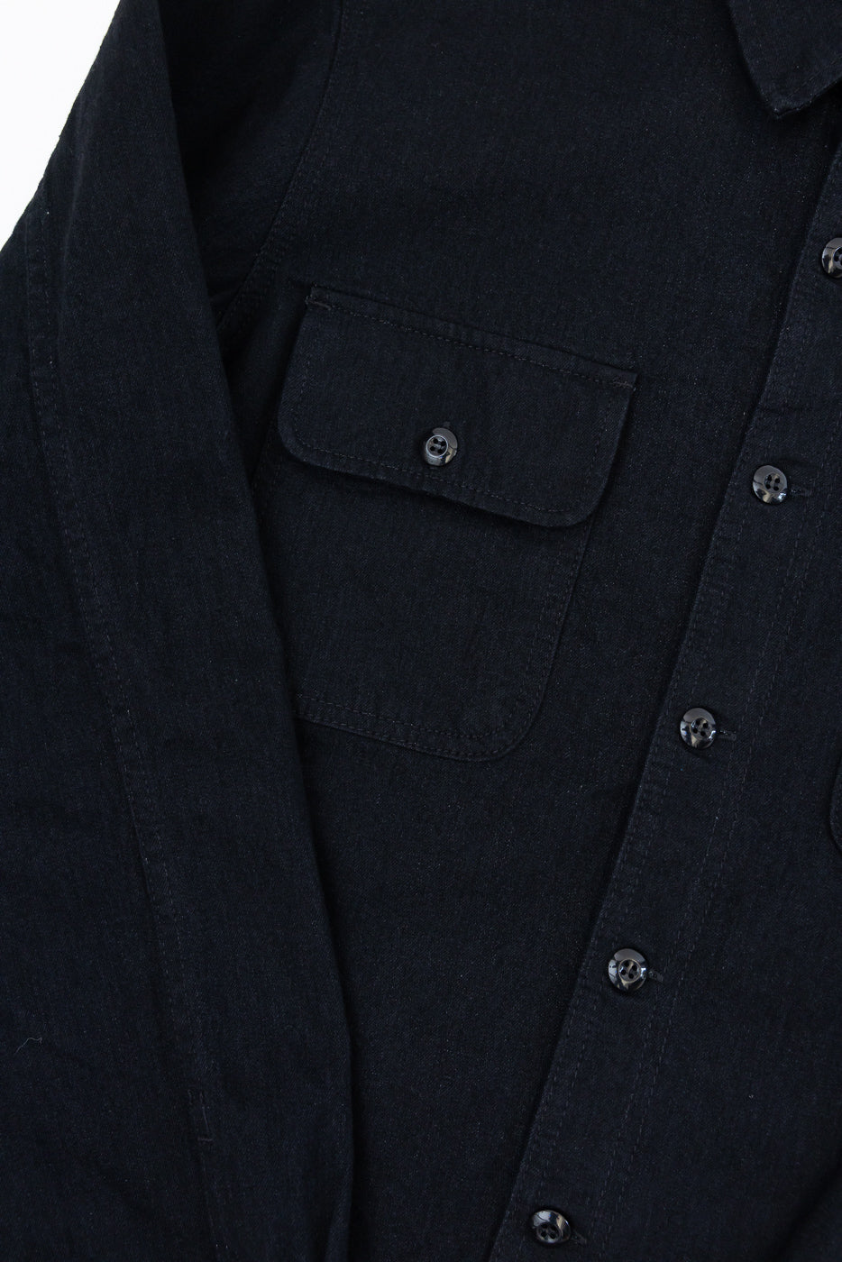 Close-up front view of black denim shirt with buttoned chest pocket and metal buttons