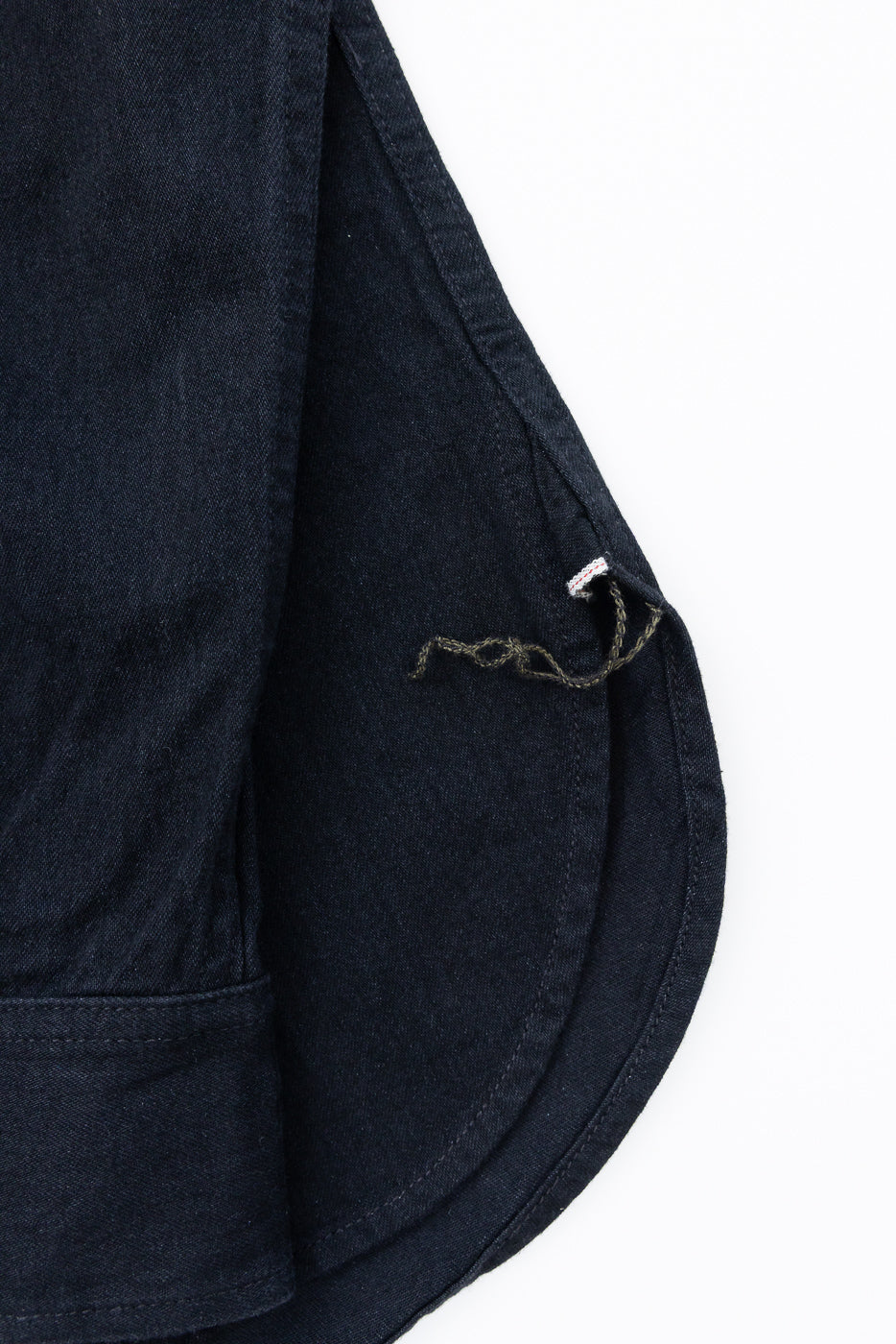 Close-up of dark denim shirt hem with detailed stitching and tag, front view