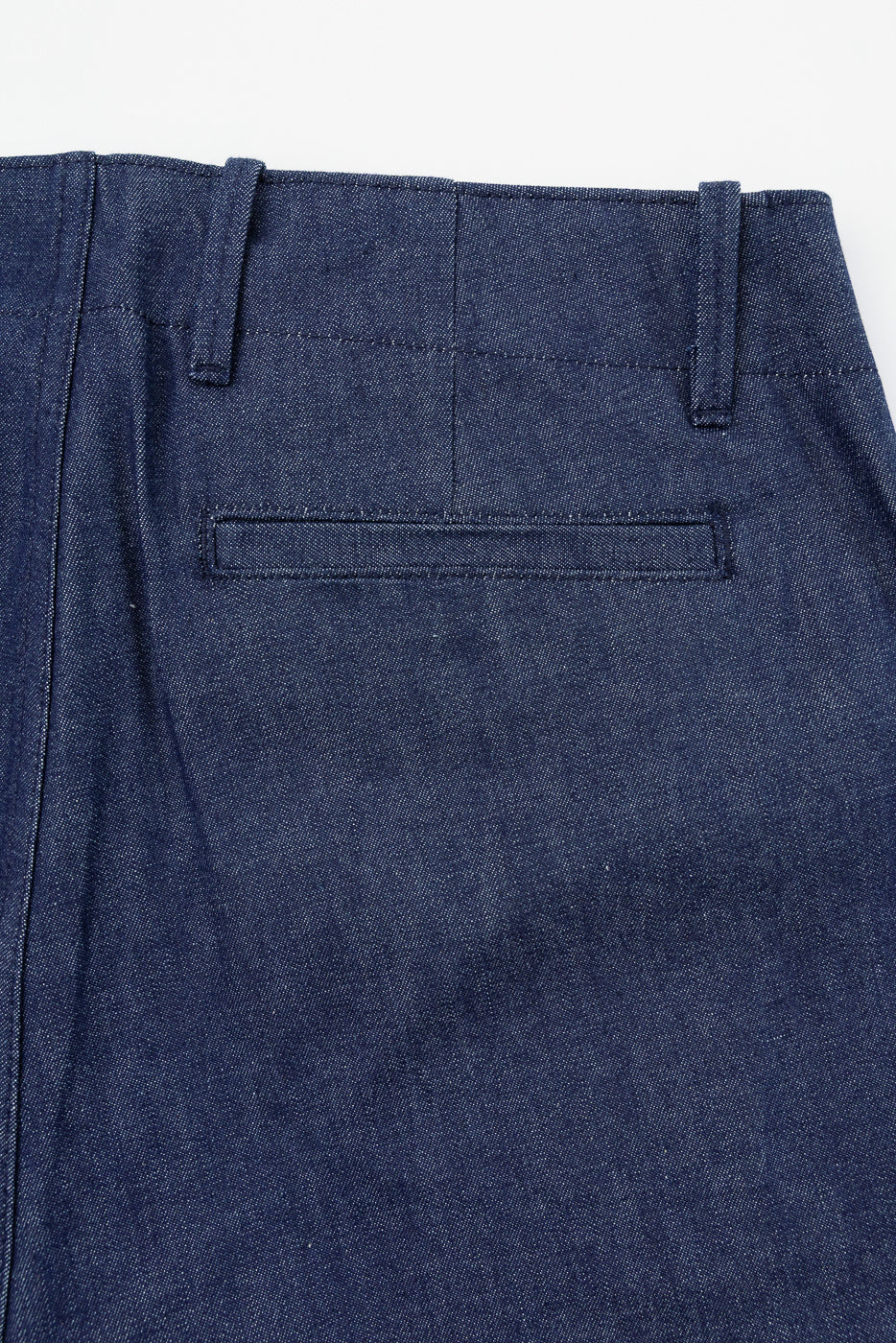 Close-up back view of dark blue selvedge chino pants, showing waistband, belt loops, and rear pocket detail