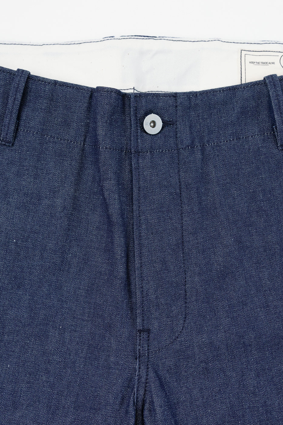 Close-up front view of dark denim pants with button fly and tag detail