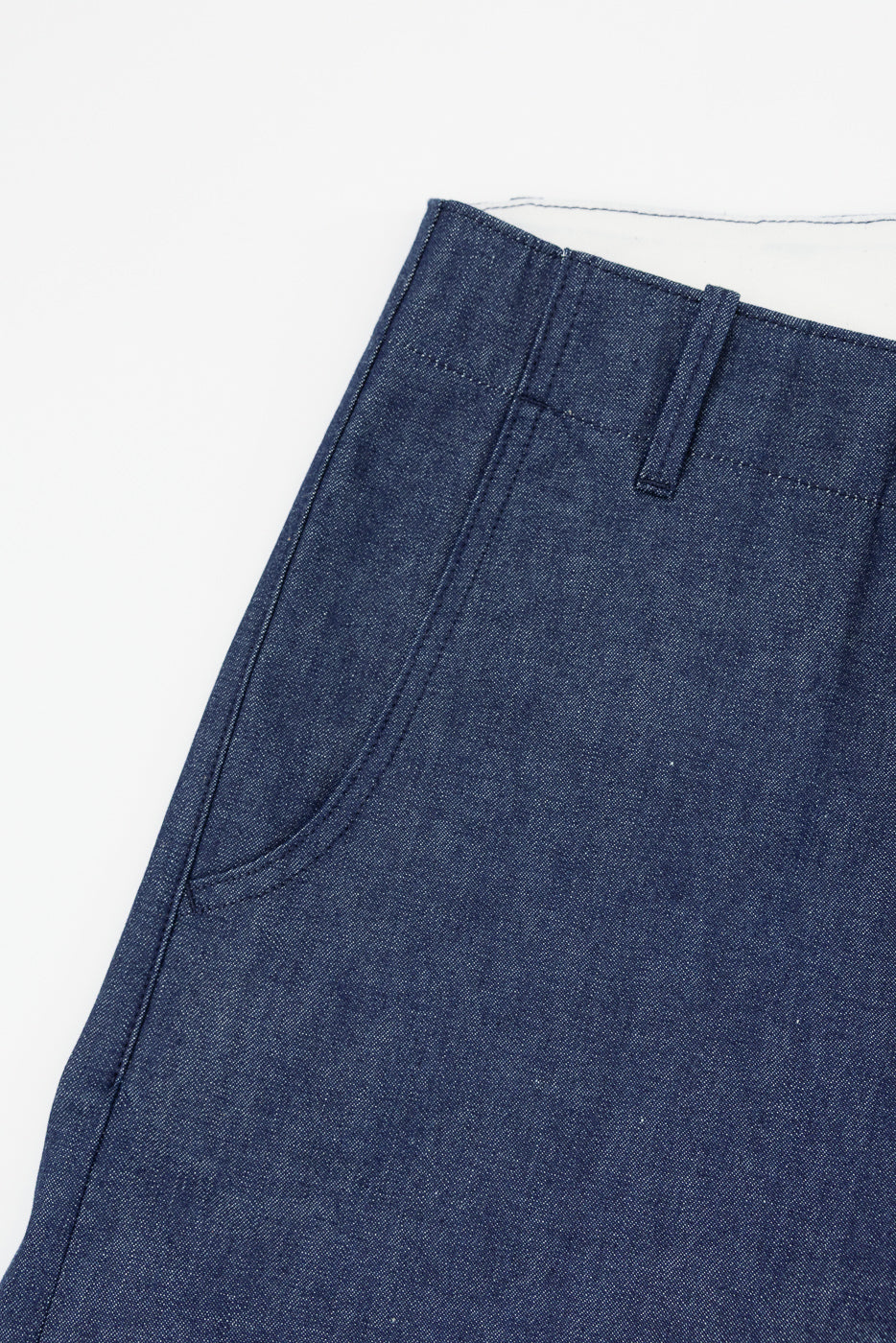 Close-up front view of dark blue selvedge denim pants, showing waistband, belt loop, and front pocket detail