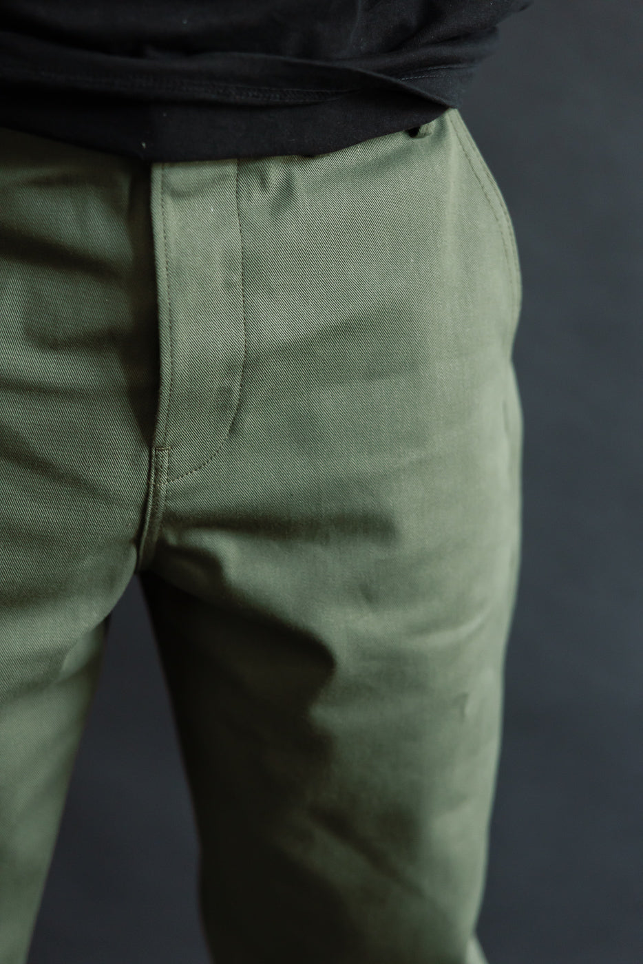 Close-up of male model's front waist and upper thighs wearing olive officer high trousers, showcasing fabric texture; model is 5'9