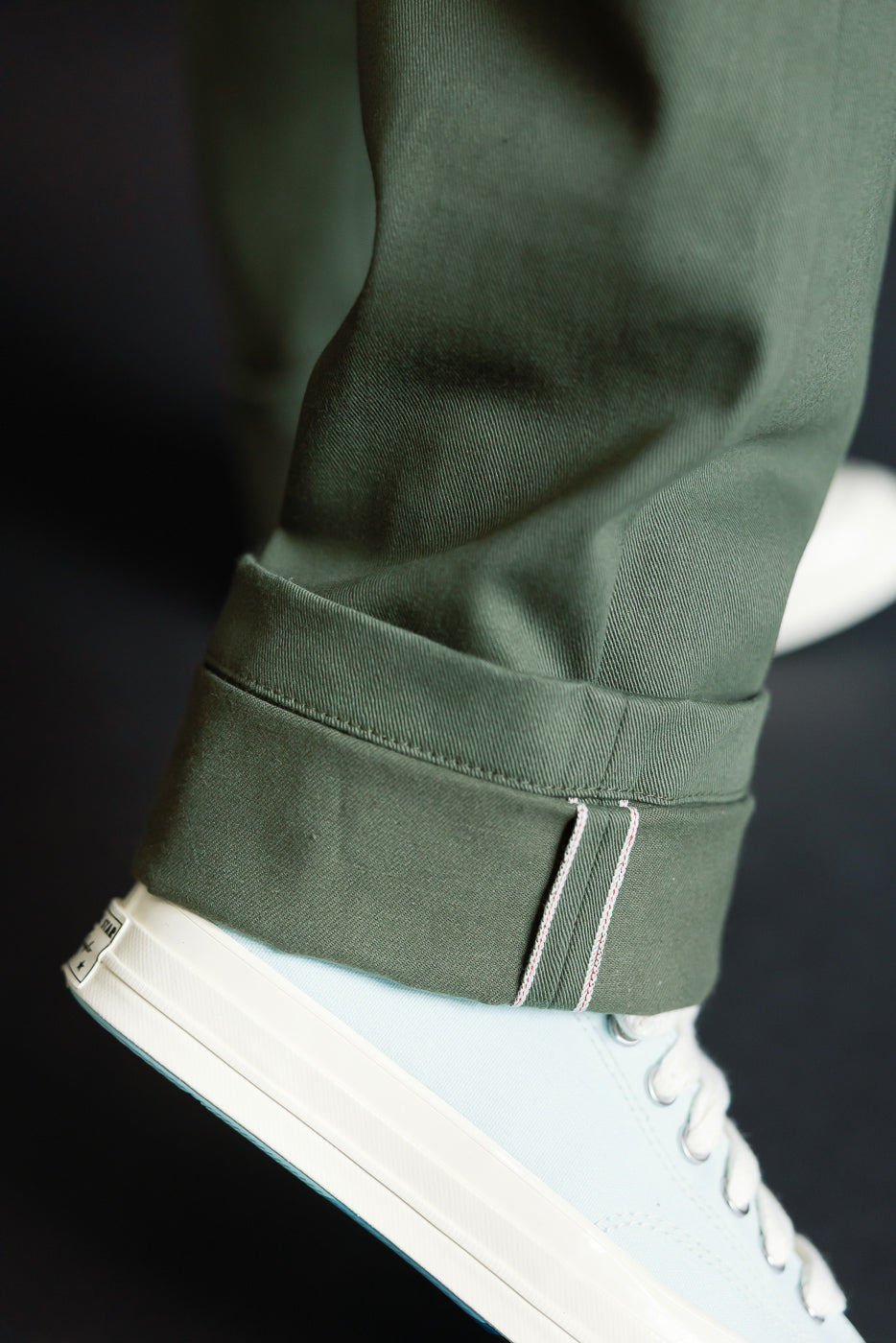 Close-up of olive officer high trouser cuff, selvedge detail, front left leg, on male model 5'9