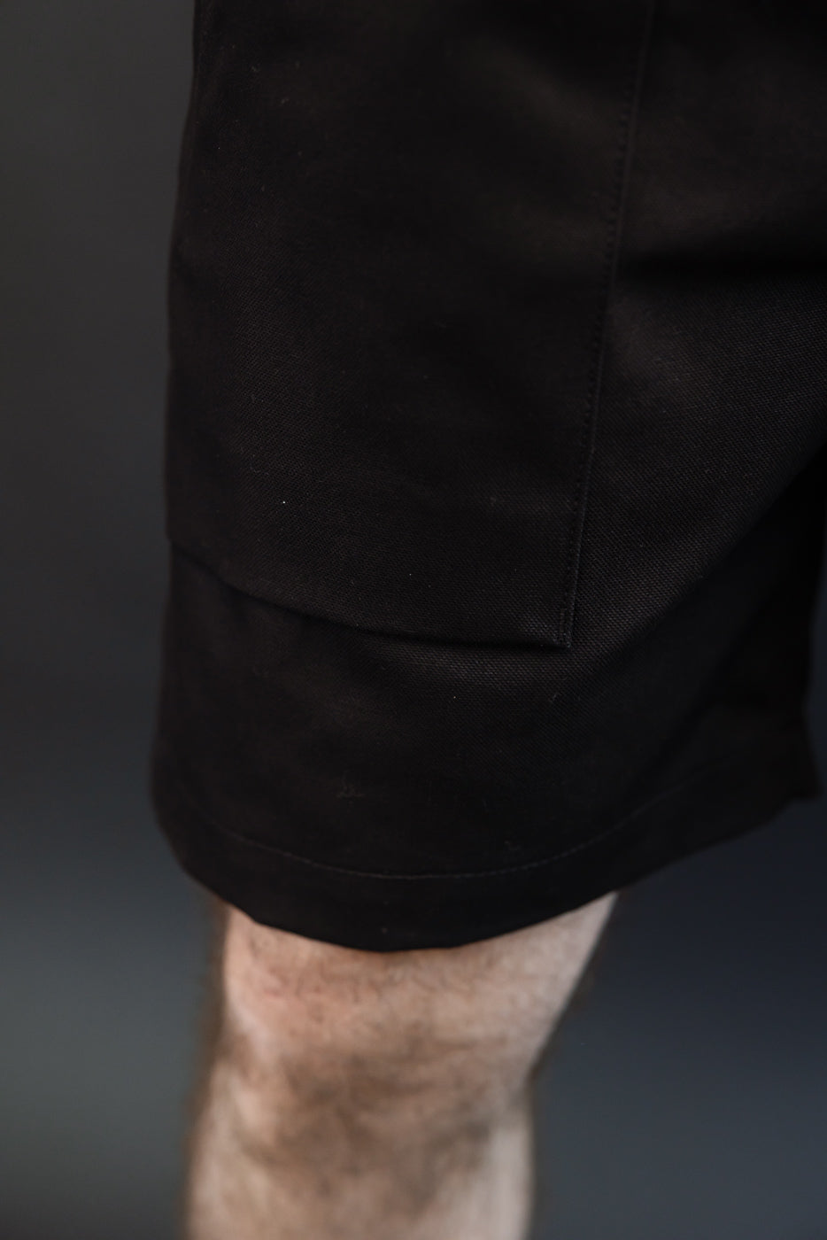 Close-up of black shorts' side pocket and hem, worn by male model with athletic build