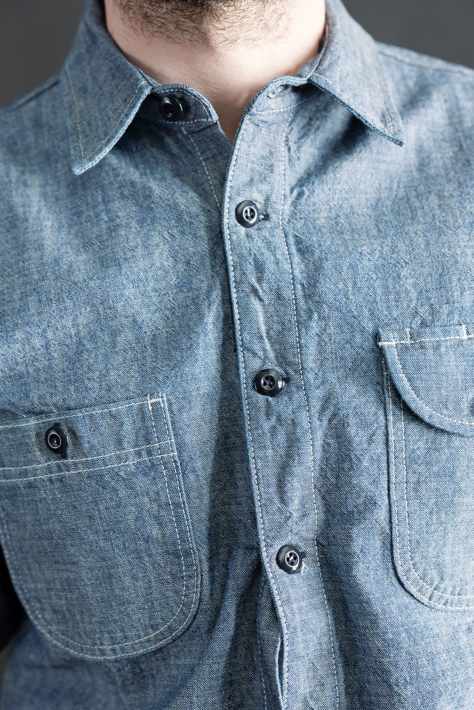 Close-up of front chest and collar of men's rinsed indigo canvas work shirt on 5'9 athletic male, showing button details, fabric texture, and dual chest pockets at Dant Indianapolis.