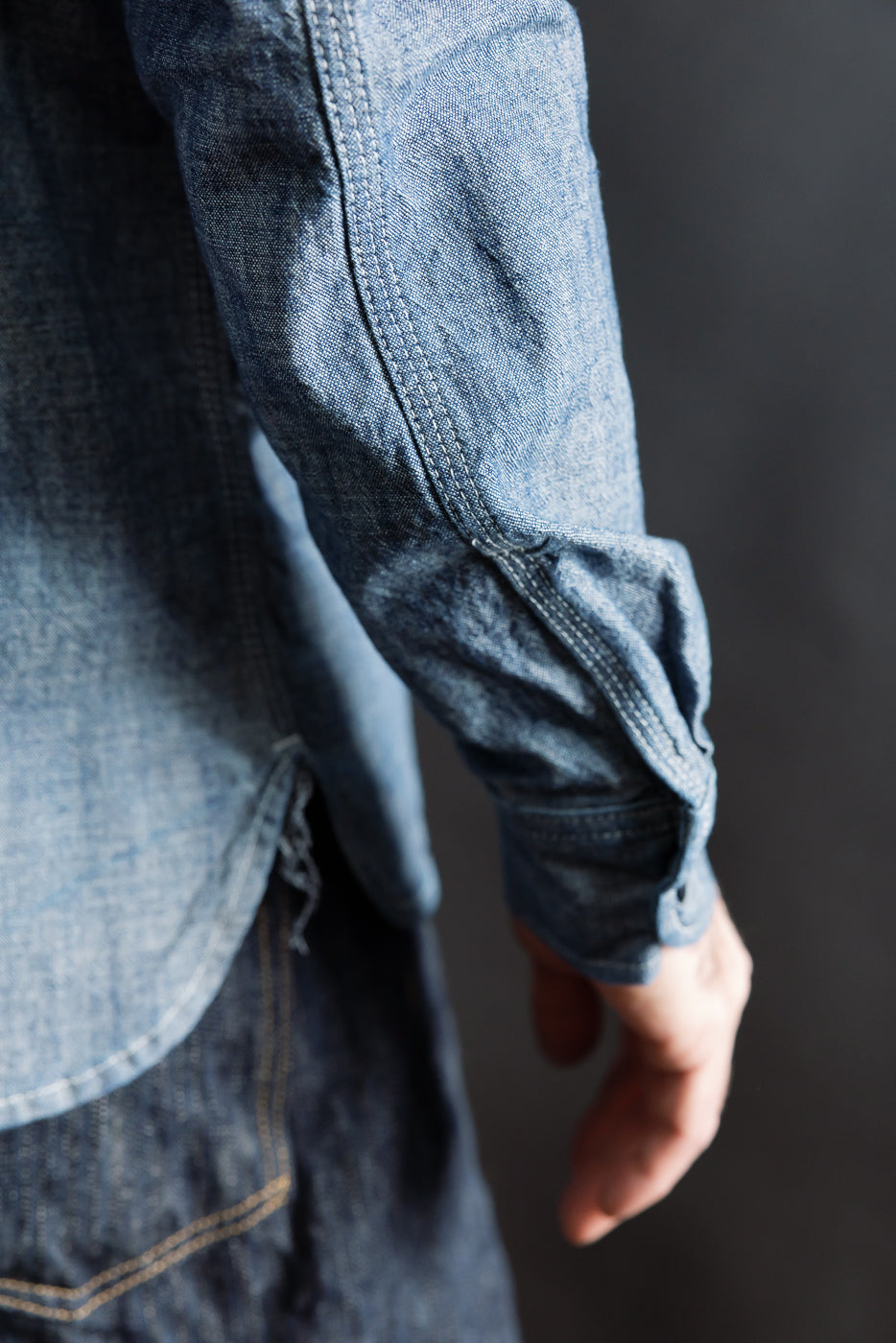 Close-up of male model's right sleeve and side seam in indigo work shirt; detailed stitching shown.