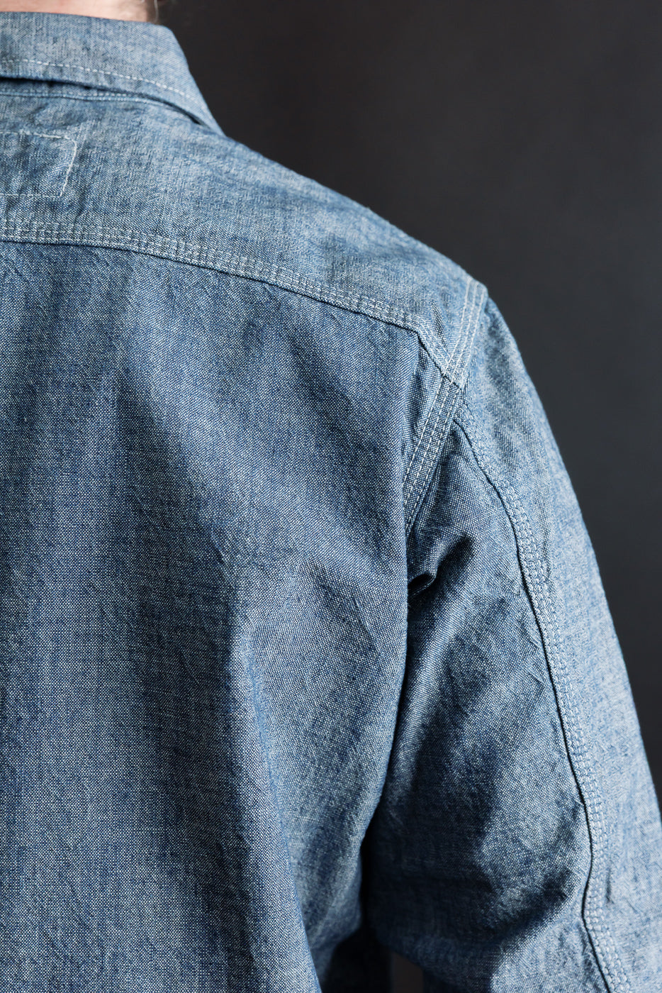 Close-up of rinsed indigo canvas work shirt, back shoulder and yoke detail, on male model