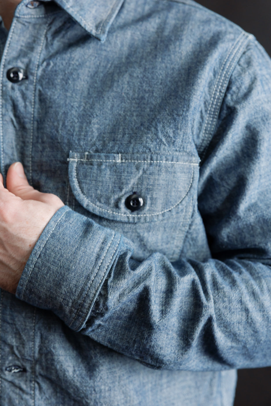 Close-up of men's indigo work shirt left chest pocket, button, and collar, athletic build model