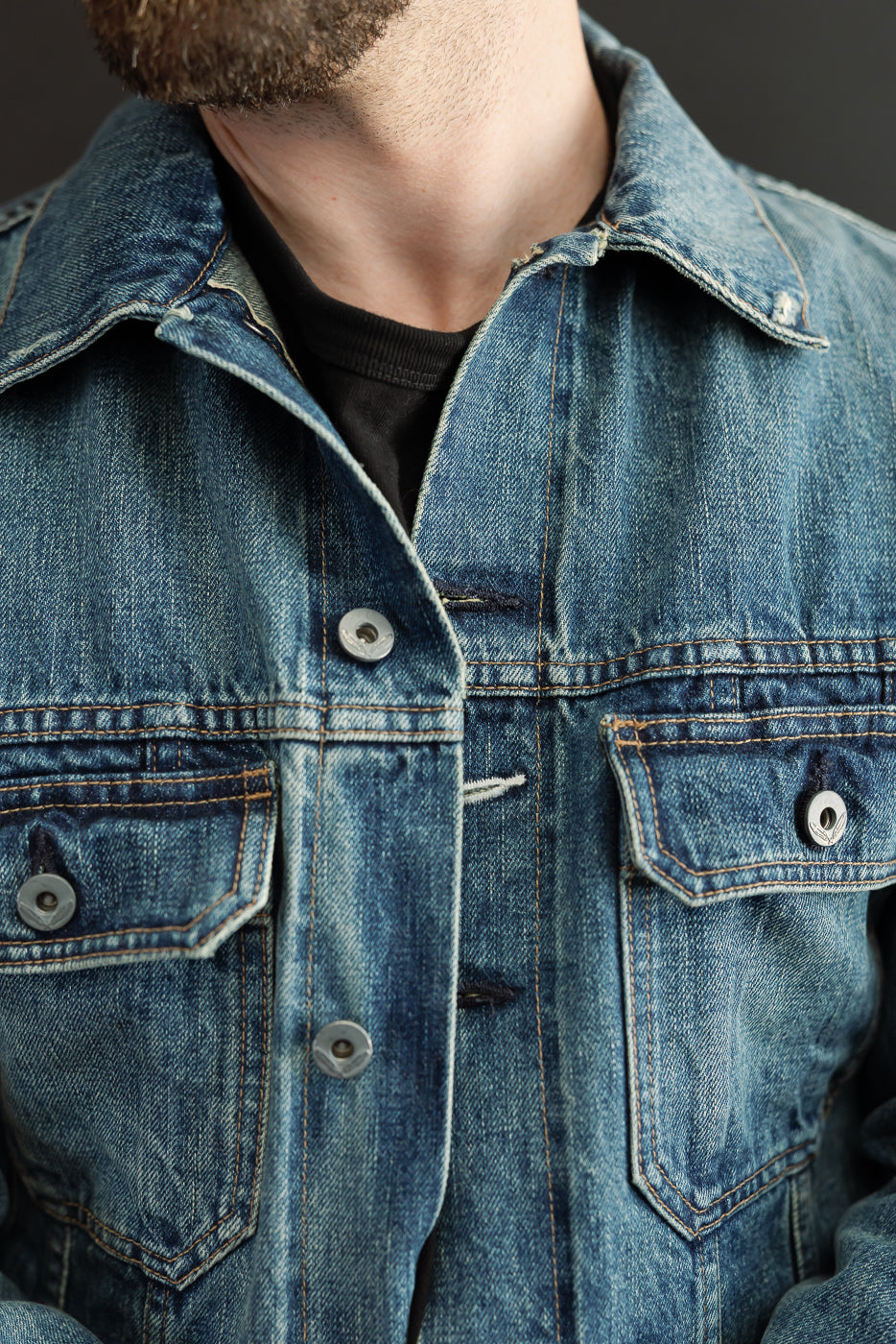 Close-up front view of male model in rugged denim jacket with button closures, chest pockets, and contrast stitching