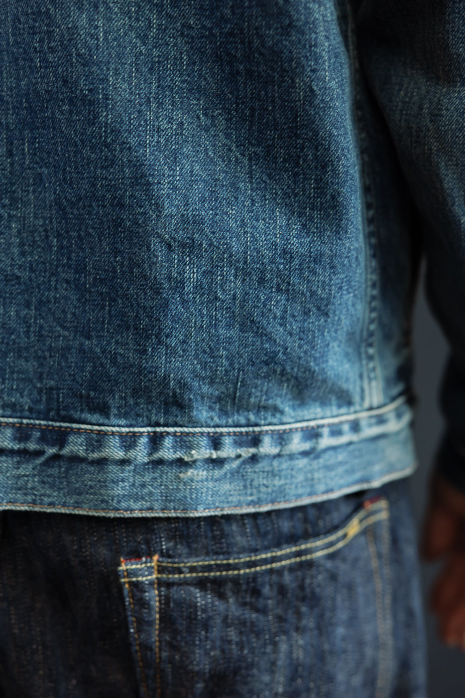 Close-up of male model's denim jacket hem and pocket, showcasing fabric texture and stitching details.