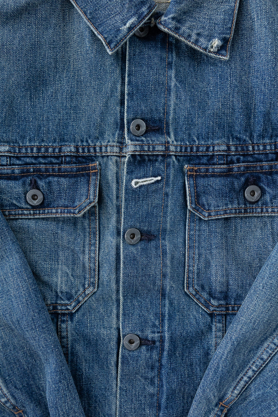 Close-up front view of men's denim jacket showing collar, buttons, chest pockets, and selvedge stitching detail
