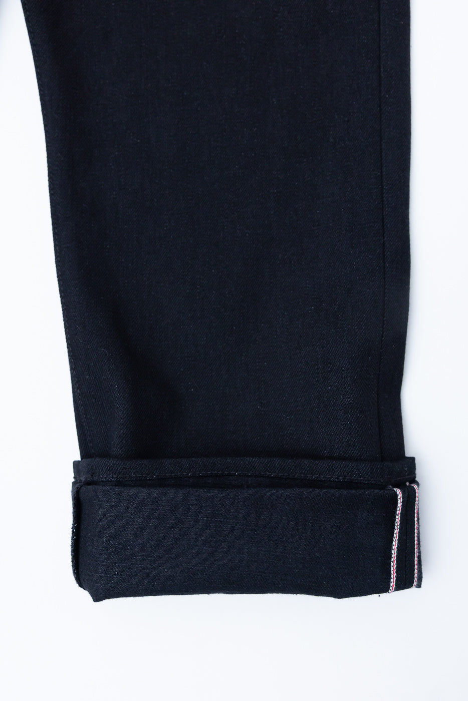 Close-up of selvedge denim pant cuff, showing hem stitching and fabric texture, side view.