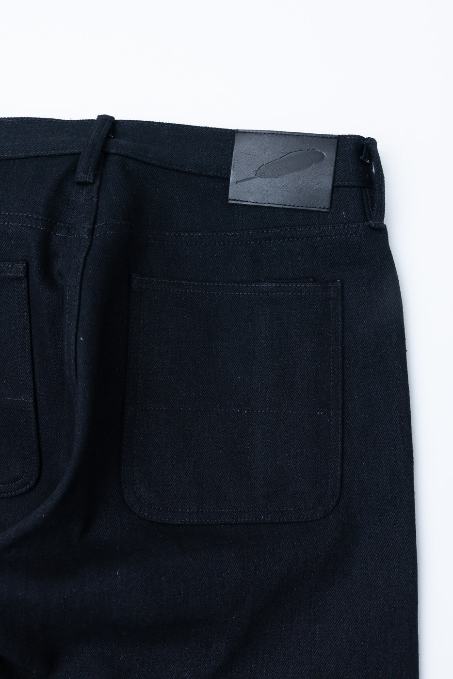 Close-up of back of dark selvedge denim jeans, showing pockets and leather patch detail.