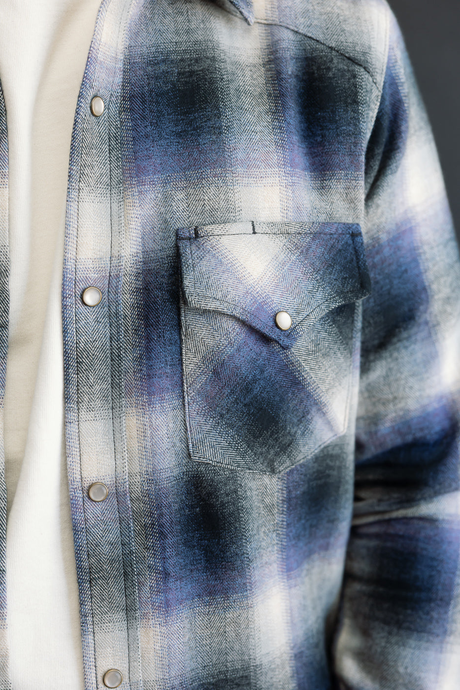 Close-up, front view of a blue and white plaid flannel shirt featuring a buttoned chest pocket.