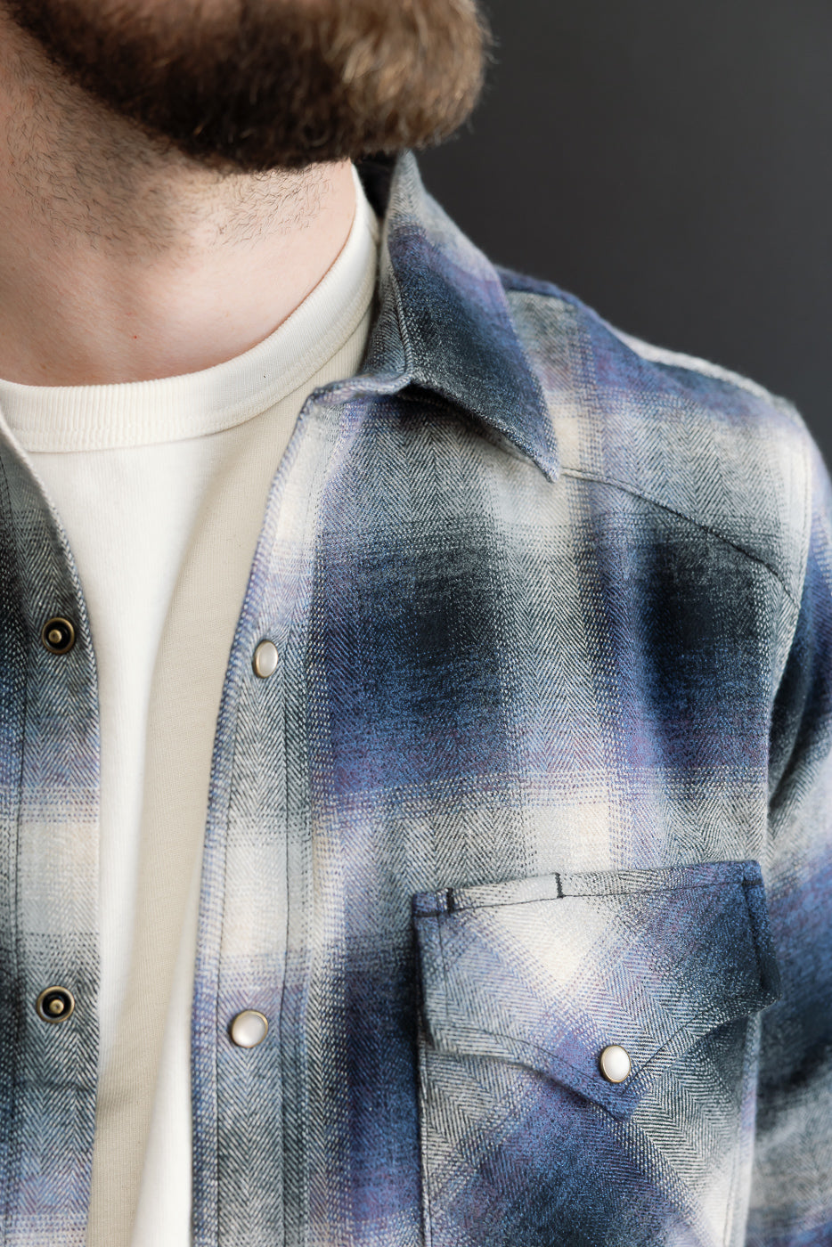 Close-up, front view of a blue and grey plaid flannel shirt on a male model, showing collar and pocket.