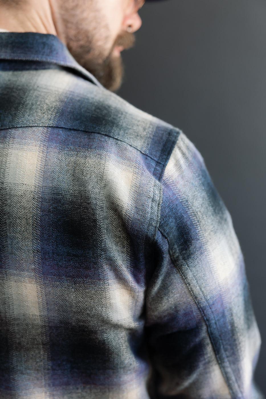 Close-up of the back and shoulder of a plaid flannel shirt on a male model.