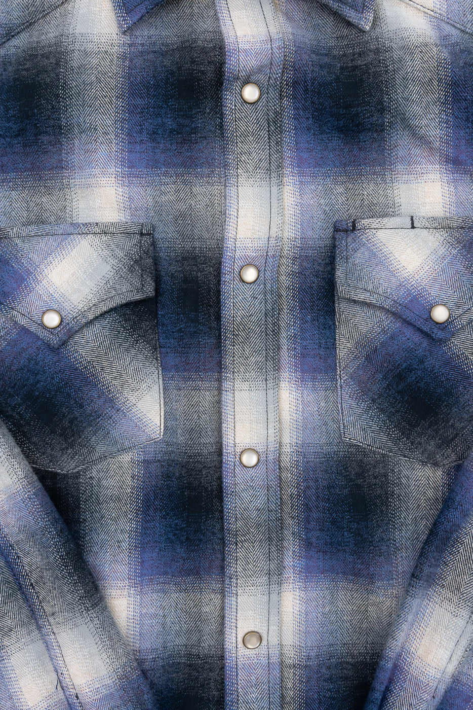 Close-up front view of a blue and grey plaid flannel shirt showing fabric texture and snap buttons.