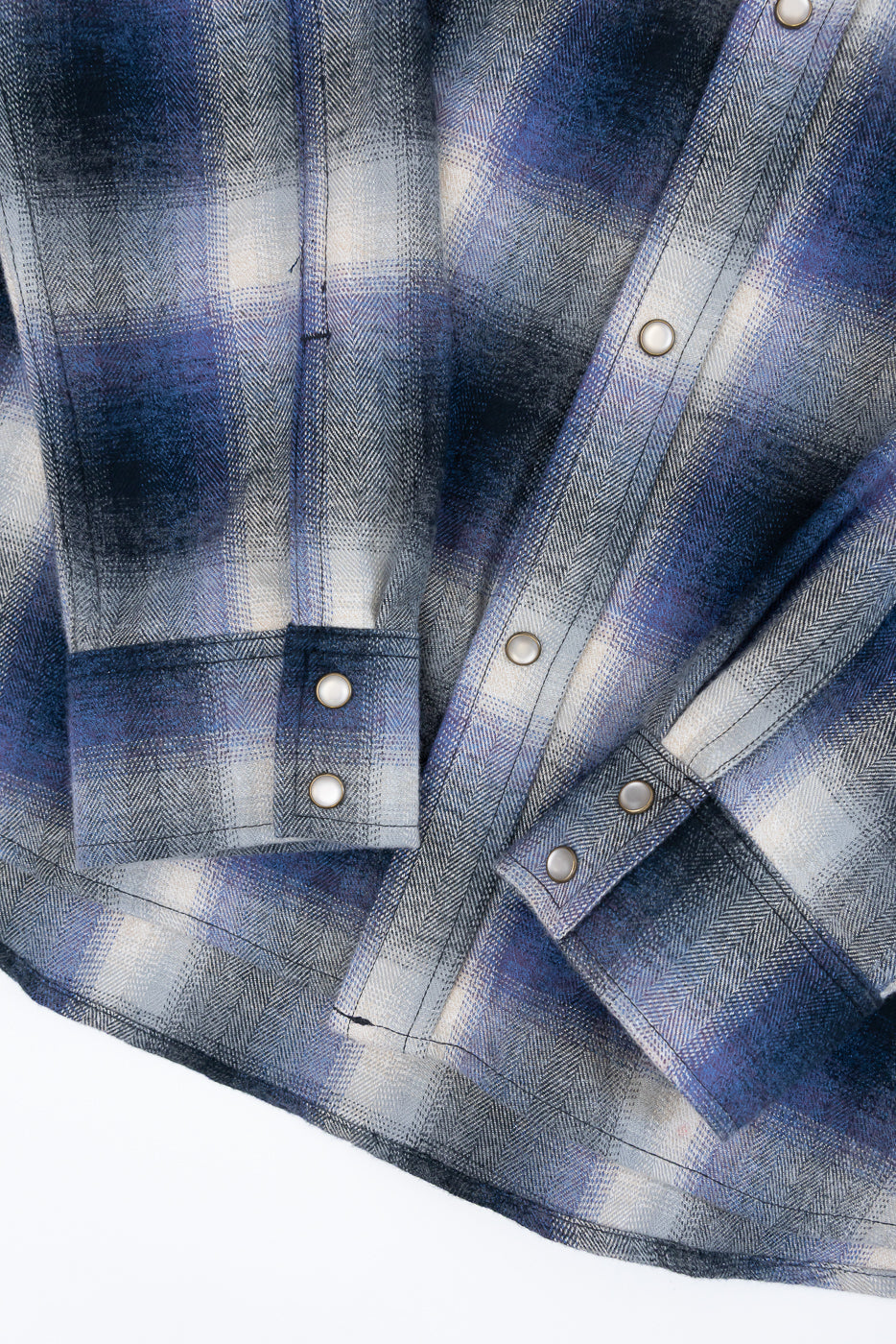 Close-up of the front cuff and button placket on a blue and grey plaid flannel shirt.