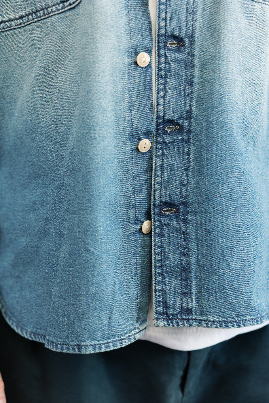 Close-up front view of men's denim shirt showing button placket, fabric texture, and hem detail