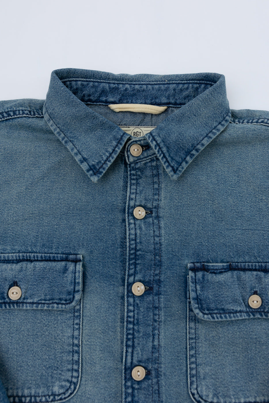 Close-up front view of men's denim shirt: button-down collar, chest pockets, RGT tag, and fabric texture detail.