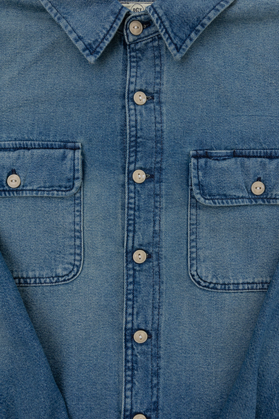 Close-up front view of men's denim shirt: button-down collar, chest pockets, and selvedge fabric texture.