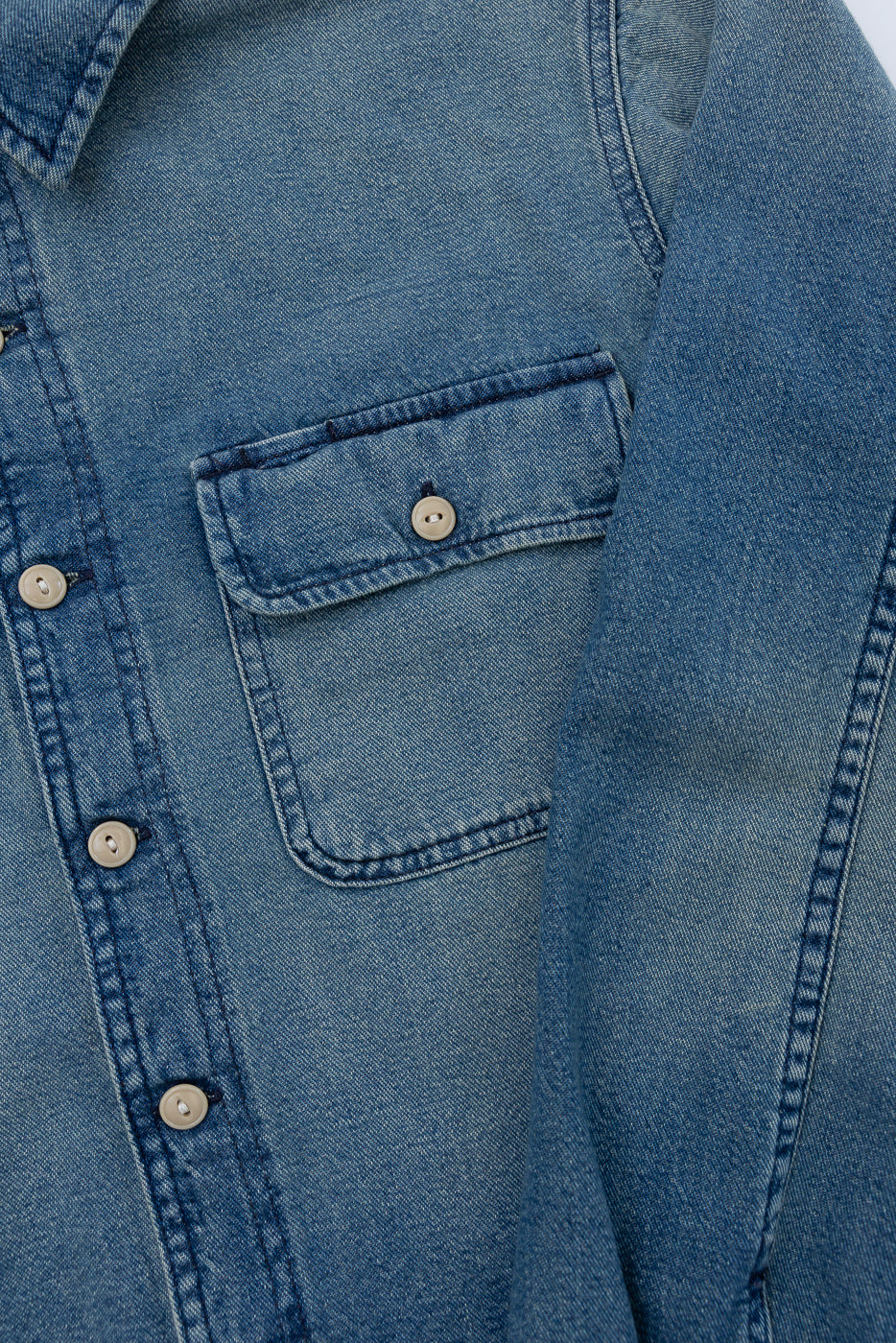 Close-up front view of men's denim shirt showing chest pocket, button closure, and fabric texture