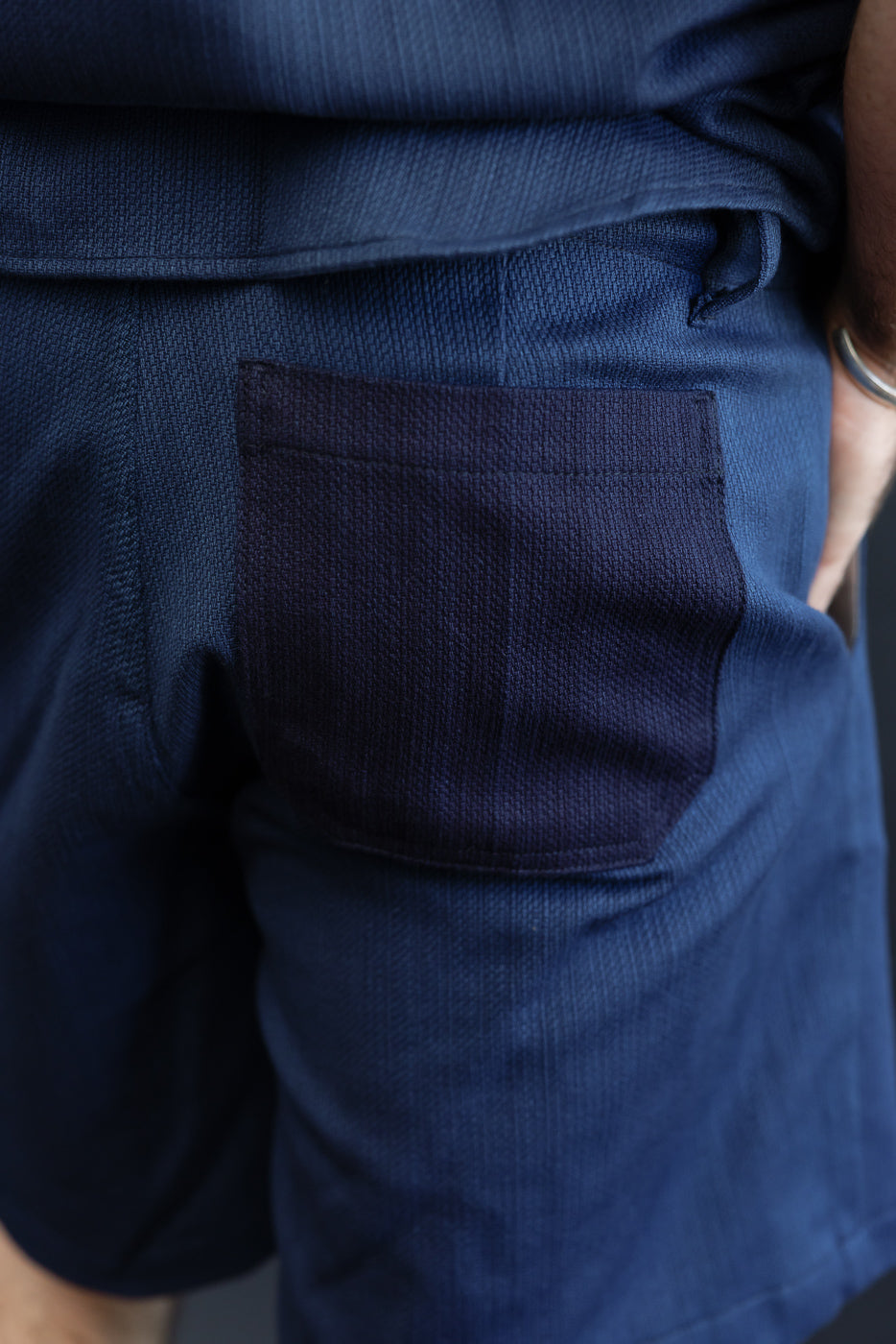 Close-up back view of navy shorts with textured fabric and rear pocket, worn by male model.